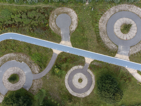 Aerial view of geometric patterns and interconnected circular structures bisected by a slender blue pathway cutting through the landscape Utopia Flevoland Netherlands.