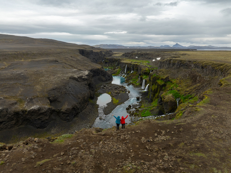 Aerial view of Sigoldugljufur canyon with its turquoise river cascading waterfalls and mossy cliffs with two people standing on the edge in Rangarthing ytra Iceland. Aerial view of Sigoldugljufur canyon with its turquoise river cascading waterfalls and mossy cliffs with two people standing on the edge in Rangarthing ytra Iceland.