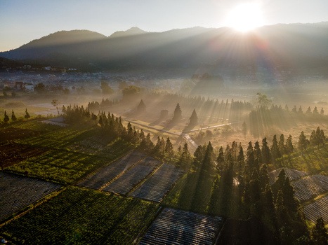 Aerial view of Dieng Plateau at sunrise with sunbeams illuminating ancient temples agricultural fields and surrounding mountains in Kecamatan Batur Jawa Tengah Indonesia. Aerial view of Dieng Plateau at sunrise with sunbeams illuminating ancient temples agricultural fields and surrounding mountains in Kecamatan Batur Jawa Tengah Indonesia.