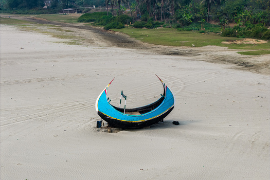 Cox s Bazar Bangladesh 10 March 2026 Aerial view of a traditional blue moon boat resting on the sandy shore with lush green palm trees and vegetation in the background. Cox s Bazar Bangladesh 10 March 2026 Aerial view of a traditional blue moon boat resting on the sandy shore with lush green palm trees and vegetation in the background.