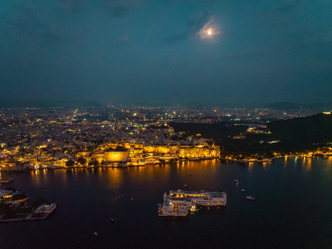 Aerial view of the illuminated City Palace and Lake Palace reflecting on the calm waters of Lake Pichola at night in Udaipur Rajasthan India.