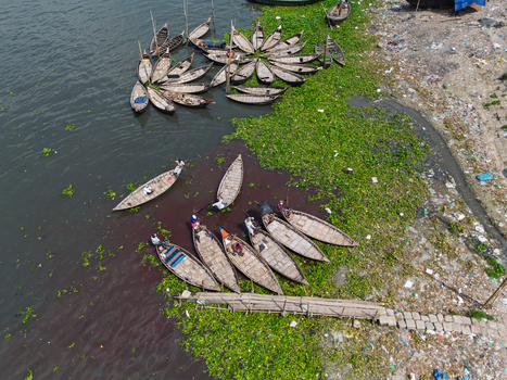 Aerial view of traditional wooden boats on the Buriganga River with green water hyacinths and people on the water in Dhaka Dhaka Division Bangladesh.