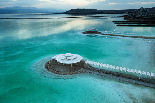 Aerial view of the serene Dead Sea s turquoise waters embrace the shoreline structures creating a striking contrast against the distant hills Ein Bokek South District Israel. Aerial view of the serene Dead Sea s turquoise waters embrace the shoreline structures creating a striking contrast against the distant hills Ein Bokek South District Israel.