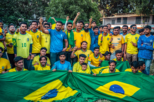 Bogura Bangladesh 18 November 2022 View of a large group of enthusiastic football fans wearing Brazil jerseys and holding a massive Brazilian flag during a public gathering.
