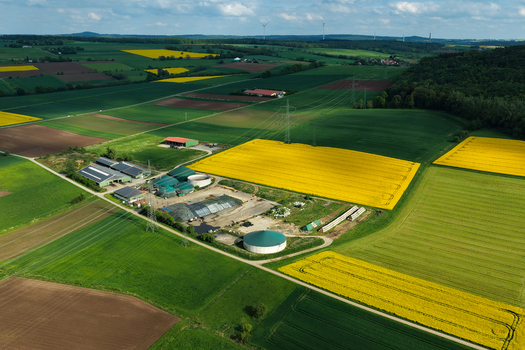 Aerial view of a biogas plant and farm buildings surrounded by vibrant yellow rapeseed fields and green meadows Hofgeismar Hessen Germany. Aerial view of a biogas plant and farm buildings surrounded by vibrant yellow rapeseed fields and green meadows Hofgeismar Hessen Germany.