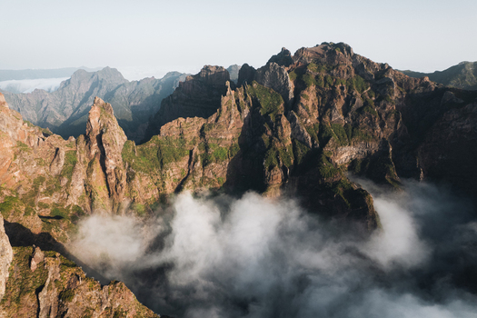 Aerial view of rugged mountain peaks piercing through a sea of ethereal clouds revealing the dramatic landscape of Pico do Areeiro Madeira Portugal.