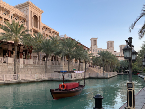View of Madinat Jumeirah featuring a traditional abra boat on a canal surrounded by palm trees and wind towers under a clear sky in Dubai Dubai United Arab Emirates. View of Madinat Jumeirah featuring a traditional abra boat on a canal surrounded by palm trees and wind towers under a clear sky in Dubai Dubai United Arab Emirates.