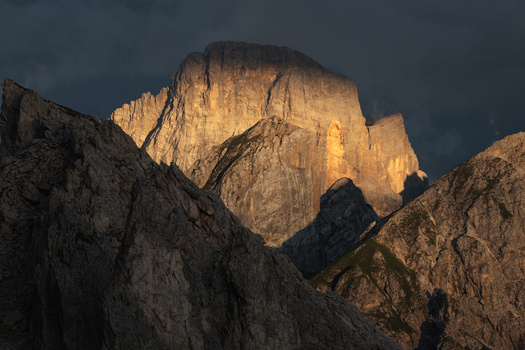 View of the Dolomites jagged peaks illuminated by golden sunset light against a dark moody sky in Trentino Alto Adige Italy. View of the Dolomites jagged peaks illuminated by golden sunset light against a dark moody sky in Trentino Alto Adige Italy.