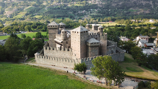 Aerial view of Fenis Castle with its medieval stone towers and fortified walls surrounded by green meadows and lush hills in Aosta Valley Aosta Valley Italy. Aerial view of Fenis Castle with its medieval stone towers and fortified walls surrounded by green meadows and lush hills in Aosta Valley Aosta Valley Italy.