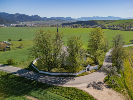 Aerial view of All Saints Church surrounded by tall trees and a circular stone wall amidst green fields and distant mountains Ludrova Zilina Region Slovakia. Aerial view of All Saints Church surrounded by tall trees and a circular stone wall amidst green fields and distant mountains Ludrova Zilina Region Slovakia.