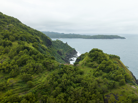 Aerial view of vibrant green Pengilon Hill slopes dramatically into the turquoise sea Gunungkidul Regency Daerah Istimewa Yogyakarta Indonesia. Aerial view of vibrant green Pengilon Hill slopes dramatically into the turquoise sea Gunungkidul Regency Daerah Istimewa Yogyakarta Indonesia.