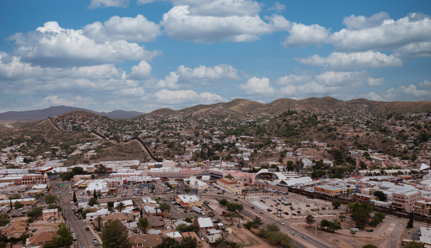 Aerial view of the international border fence separating the city from the hills with urban buildings streets and clouds in Nogales Arizona United States.
