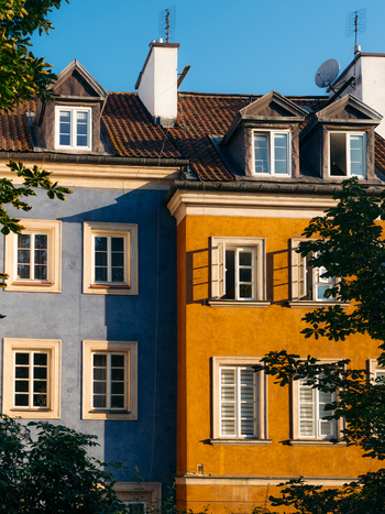 View of colorful historic buildings in Warsaw Old Town featuring blue and yellow facades classic windows and lush green trees under a clear sky in Warsaw Masovian Voivodeship Poland. View of colorful historic buildings in Warsaw Old Town featuring blue and yellow facades classic windows and lush green trees under a clear sky in Warsaw Masovian Voivodeship Poland.