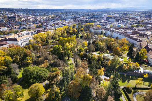 Aerial view of a vibrant park with trees displaying autumn colors contrasting against the urban landscape and the distant mountains Graz Styria Austria.