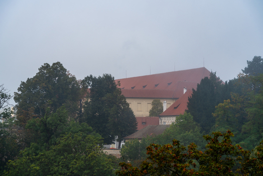 View of a historic building with a red tiled roof nestled among lush trees under a misty sky in Prague Prague Czechia.