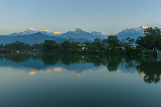 Aerial view of Phewa Lake with the Annapurna mountain range reflecting in the calm water at sunset in Pokhara Nepal.
