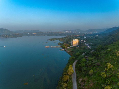 Aerial view of a serene lake surrounded by lush green hills and a coastal road in Udaipur Rajasthan India. Aerial view of a serene lake surrounded by lush green hills and a coastal road in Udaipur Rajasthan India.