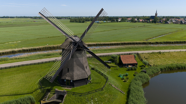 Aerial view of Bovenmolen G a historic windmill with a thatched roof set in a lush green landscape with canals and a small road in Schermerhorn Noord Holland Netherlands. Aerial view of Bovenmolen G a historic windmill with a thatched roof set in a lush green landscape with canals and a small road in Schermerhorn Noord Holland Netherlands.