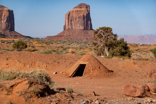 View of a traditional Navajo hogan set against the iconic red sandstone buttes of Monument Valley Tribal Park in the desert landscape of Oljato Monument Valley Utah United States.