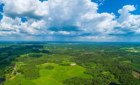 Aerial view of lush green forests and open fields under a dramatic sky with large white clouds in Latvia. Aerial view of lush green forests and open fields under a dramatic sky with large white clouds in Latvia.