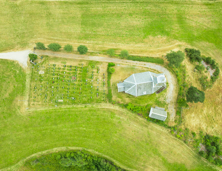 Aerial view of the historic church and cemetery surrounded by green fields and trees in Araksbo Agder Norway.