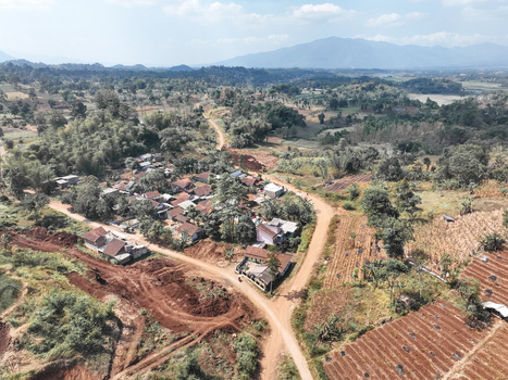 Aerial view of a small rural village surrounded by terraced agricultural fields dirt roads and lush green hills in Garut West Java Indonesia. Aerial view of a small rural village surrounded by terraced agricultural fields dirt roads and lush green hills in Garut West Java Indonesia.
