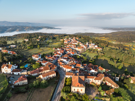 Aerial view of Vila Pouca da Beira with red tiled roofs surrounded by lush green hills and morning fog in the valley Vila Pouca da Beira Coimbra Portugal.