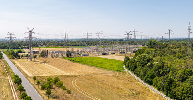 Aerial view of the Amprion Umspannwerk electrical substation with high voltage power lines and pylons surrounded by agricultural fields and forests in Pfungstadt Hessen Germany.