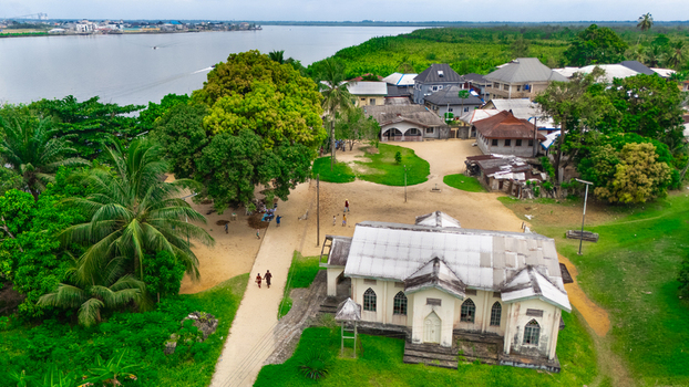 Aerial view of a church building situated near a riverbank surrounded by lush greenery palm trees and sandy paths in Minima Rivers Nigeria.