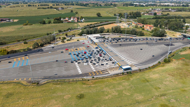 Aerial view of the Milano Sud toll plaza on the A1 motorway with vehicles passing through lanes surrounded by agricultural fields and highway infrastructure in Melegnano Lombardy Italy.