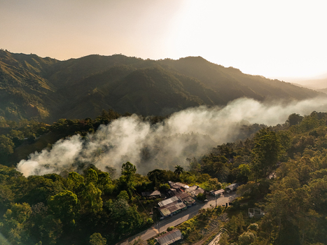 Aerial view of smoke rising from a forest fire near a road and small buildings in the mountainous landscape of Jarabacoa La Vega Province Dominican Republic.