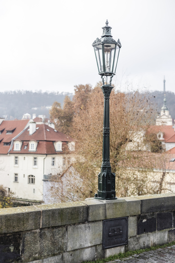 View of a vintage street lamp on a stone wall with historic red roofed buildings and autumn foliage in Prague Prague Czechia. View of a vintage street lamp on a stone wall with historic red roofed buildings and autumn foliage in Prague Prague Czechia.