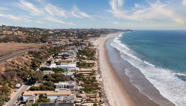 Aerial view of the coastline in Malibu featuring luxury beachfront homes a sandy beach Pacific Ocean waves and a coastal highway in Malibu California United States.