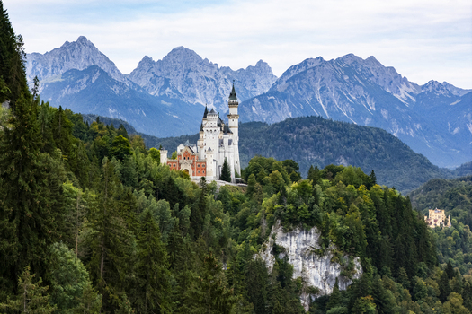 Aerial view of Neuschwanstein Castle perched majestically atop a verdant hill framed by the rugged snow capped Alps creating a fairytale scene Neuschwanstein Bayern Germany. Aerial view of Neuschwanstein Castle perched majestically atop a verdant hill framed by the rugged snow capped Alps creating a fairytale scene Neuschwanstein Bayern Germany.