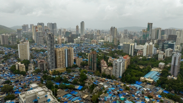 Aerial view of Dharavi Slums with its dense blue roofed structures contrasting against the modern high rise skyline of Mumbai Maharashtra India. Aerial view of Dharavi Slums with its dense blue roofed structures contrasting against the modern high rise skyline of Mumbai Maharashtra India.