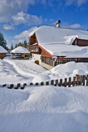View of a snow covered chalet glows warmly under a blue sky contrasting with the pristine white landscape Donovaly Banskobystricky kraj Slovakia. View of a snow covered chalet glows warmly under a blue sky contrasting with the pristine white landscape Donovaly Banskobystricky kraj Slovakia.