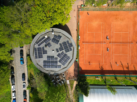 Aerial view of a circular building with solar panels on the roof next to clay tennis courts with players and green trees in Woluwe Saint Lambert Bruxelles Belgium. Aerial view of a circular building with solar panels on the roof next to clay tennis courts with players and green trees in Woluwe Saint Lambert Bruxelles Belgium.