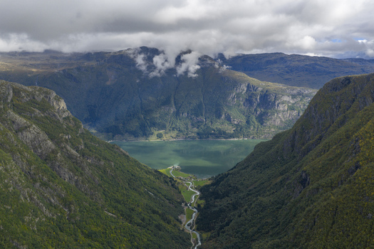 Aerial view of Sandvinvatnet lake nestled between steep mountain slopes with a winding river and low clouds in Ullensvang Vestland Norway.