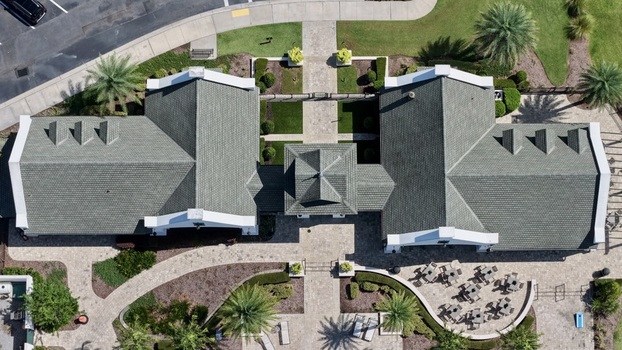 Aerial view of the Windward Ranch clubhouse featuring a green shingled roof stone paved walkways lush palm trees and an outdoor seating area in St. Johns County Florida United States. Aerial view of the Windward Ranch clubhouse featuring a green shingled roof stone paved walkways lush palm trees and an outdoor seating area in St. Johns County Florida United States.