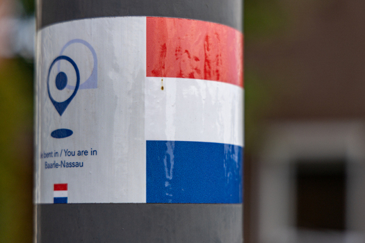 View of a sign on a pole featuring the Dutch flag and text indicating the location in Baarle Nassau North Brabant Netherlands.