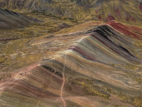 Aerial view of Vinicunca Rainbow Mountain showing its vibrant mineral stripes and hikers on the trail under the sunlight in Quispicanchi Province Cusco Peru.