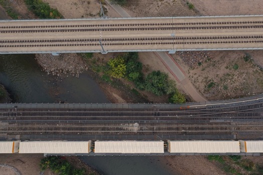 Aerial view of two parallel railway bridges crossing a river with a freight train passing over one of them surrounded by trees and a path in Denver Colorado United States. Aerial view of two parallel railway bridges crossing a river with a freight train passing over one of them surrounded by trees and a path in Denver Colorado United States.