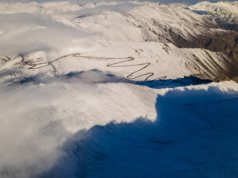 Aerial view of Babusar Pass with its winding road snaking through snow covered mountain peaks under a layer of clouds Babusar KPK Pakistan.