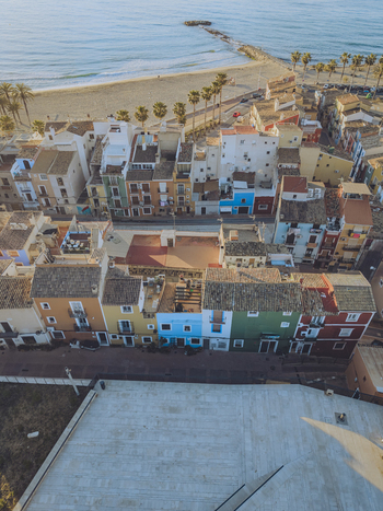 Aerial view of colorful houses along the coast with a sandy beach and palm trees under soft sunlight in La Vila Joiosa Valencian Community Spain. Aerial view of colorful houses along the coast with a sandy beach and palm trees under soft sunlight in La Vila Joiosa Valencian Community Spain.