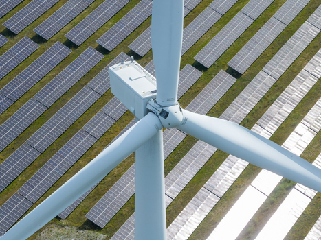 Aerial view of a large wind turbine standing in the middle of a vast solar farm with rows of photovoltaic panels in a green field Poland.