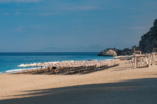 View of straw umbrellas line the beach against the turquoise sea and rugged cliffs a serene landscape basking in the sunlight Lefkada Greece. View of straw umbrellas line the beach against the turquoise sea and rugged cliffs a serene landscape basking in the sunlight Lefkada Greece.
