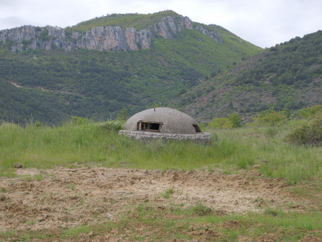 View of a concrete bunker situated in a grassy field with rugged mountains in the background in Pogradec Korce County Albania. View of a concrete bunker situated in a grassy field with rugged mountains in the background in Pogradec Korce County Albania.