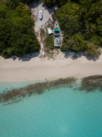 Aerial view of boats resting on the sandy shore framed by lush greenery and turquoise waters Vashafaru Island Maldives.