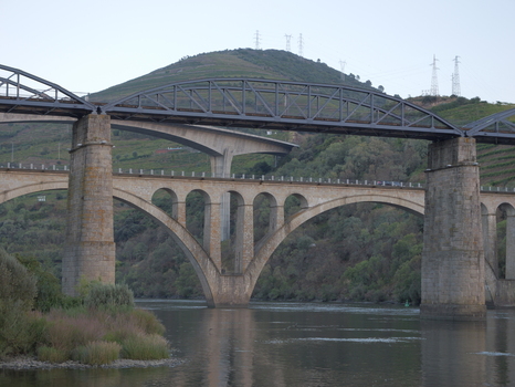View of the historic stone arch bridge and steel truss bridge spanning the Douro River with vineyards on the hills in the background in Peso da Regua Vila Real District Portugal.