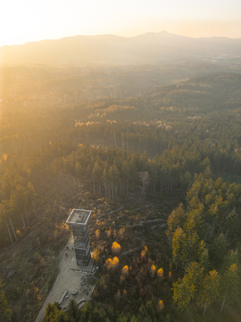 Aerial view of Cisaruv kamen lookout tower surrounded by dense coniferous forests and rolling hills during a golden sunset in Liberec Liberec Region Czechia. Aerial view of Cisaruv kamen lookout tower surrounded by dense coniferous forests and rolling hills during a golden sunset in Liberec Liberec Region Czechia.
